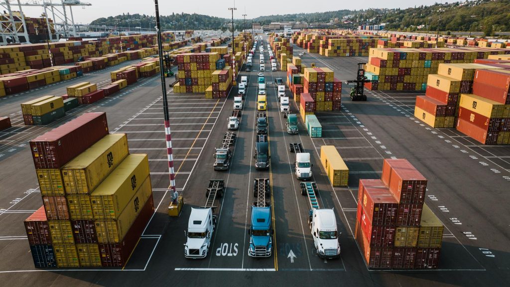 A bustling aerial shot of Seattle's shipping port with trucks lined up amongst colorful cargo containers.